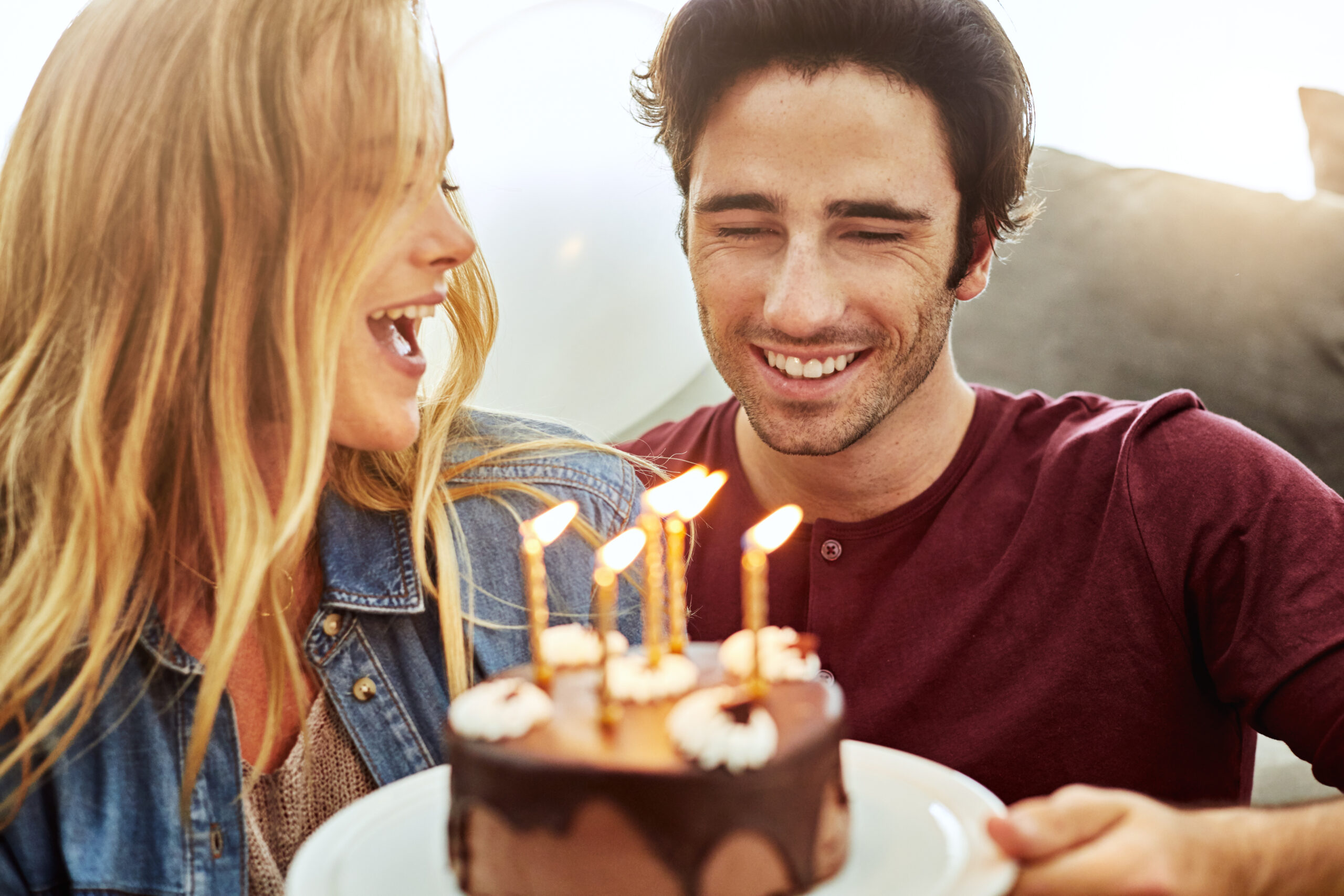 Shot of a cheerful young couple holding a birthday cake together while being seated on the floor at home
